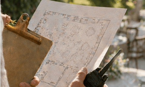 Hands holding a printed floor plan and a two-way radio, an outdoor venue setup beyond